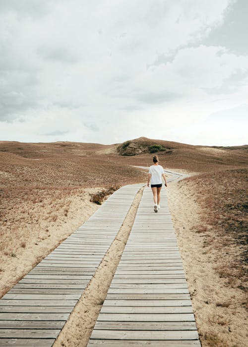 白衬衫和蓝色牛仔牛仔裤，棕色木制通路上行走的女人 · 免费素材图片