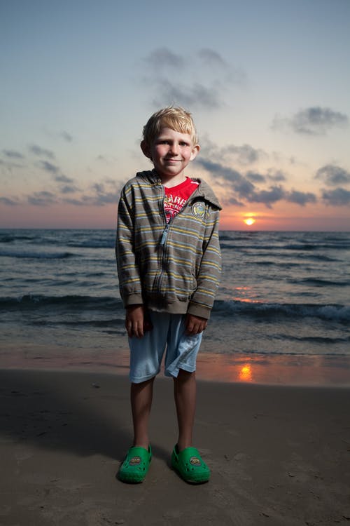 站在海滩上的灰色和黑色条纹连帽衫的男孩 · 免费素材图片