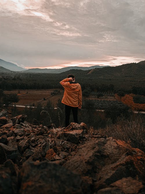 棕色外套站在绿草如茵的球场附近的棕色岩石上的女人 · 免费素材图片
