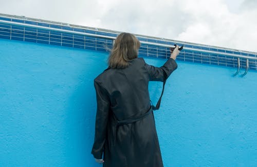 黑色外套站在蓝色的墙壁附近的女人 · 免费素材图片