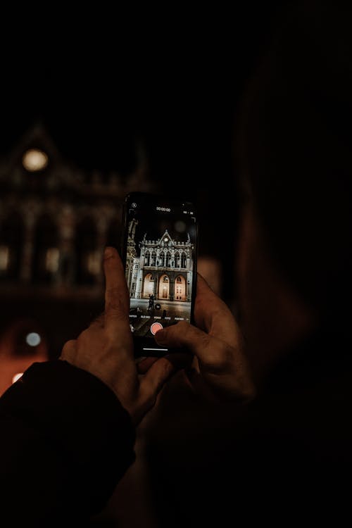 拿着智能手机的人在夜间拍摄建筑物的照片 · 免费素材图片