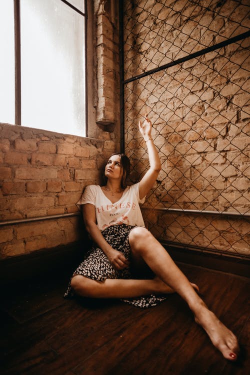 女人坐在玻璃窗旁边的地板上 · 免费素材图片