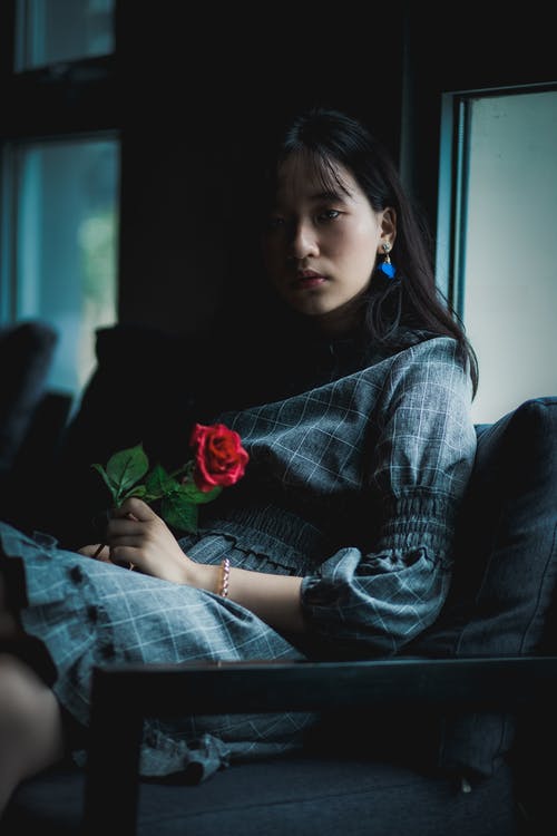 女人穿着灰色的衣服，坐在沙发上抱着红玫瑰 · 免费素材图片