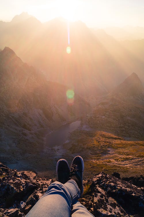 穿着黑色运动鞋坐在山上的人 · 免费素材图片
