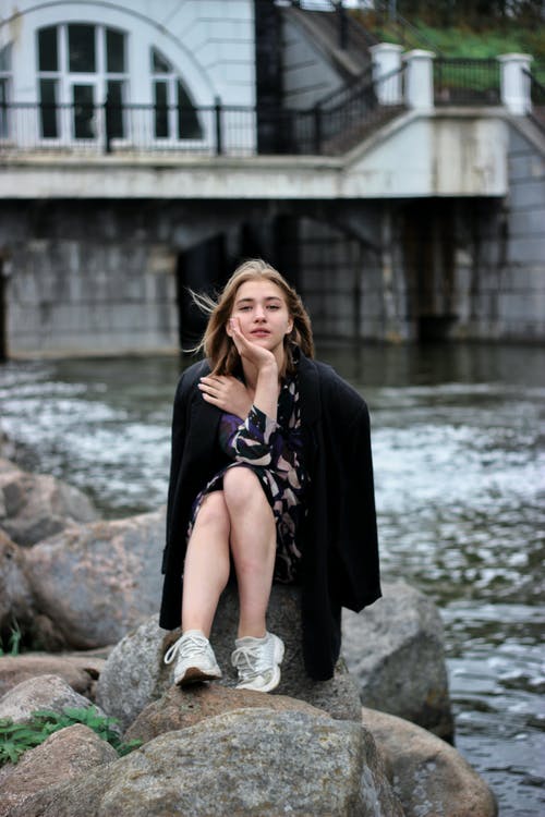黑色长袖穿裙子坐在河边的岩石上的女人 · 免费素材图片