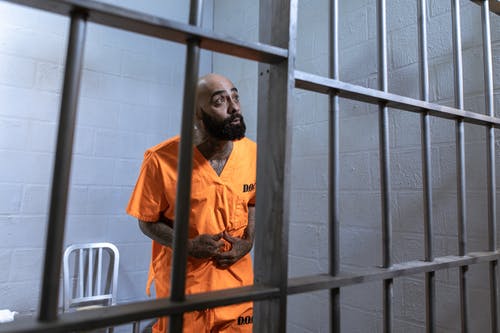 站在白色金属门旁边的衬衫的橙色按钮的人 · 免费素材图片