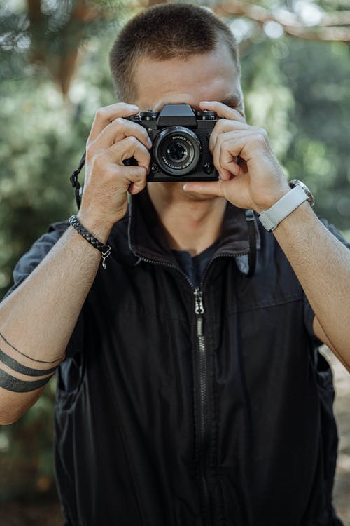 黑色拉链的背心，拿着黑色相机的人 · 免费素材图片