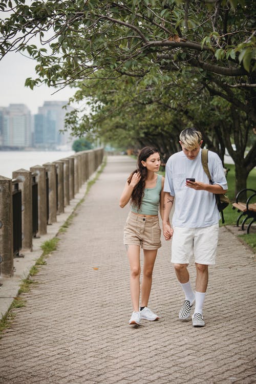 在河边公园散步时使用智能手机的年轻时尚夫妇 · 免费素材图片