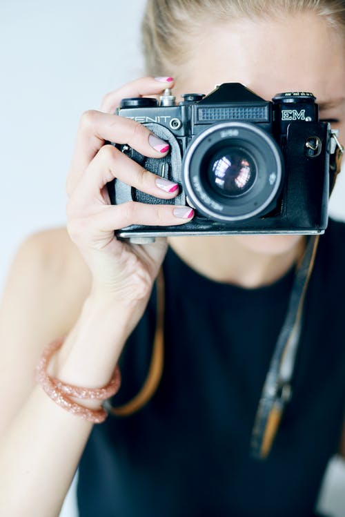 拿着黑色和银色尼康单反相机的黑色背心的女人 · 免费素材图片