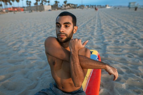 裸照男子坐在海滩上的红色冲浪板 · 免费素材图片