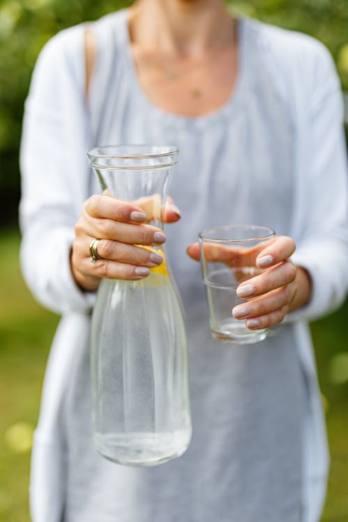 拿着水的透明玻璃瓶的白色长袖衬衫的女人 · 免费素材图片