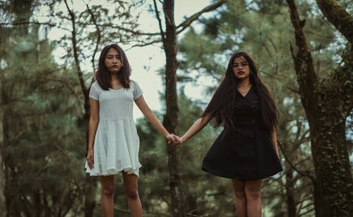 女孩穿着白色连衣裙，手牵着手，身穿黑色礼服的女孩 · 免费素材图片