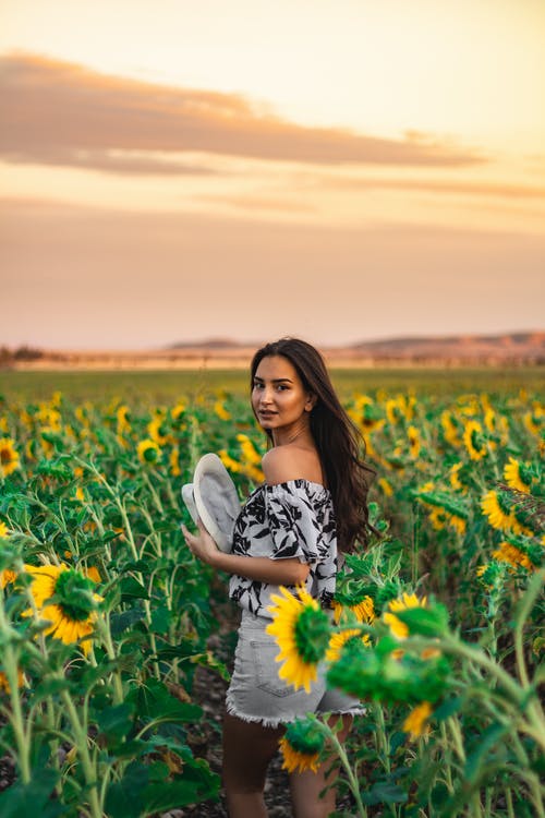 坐在黄色花田上的白色和黑色的花裙子的女人 · 免费素材图片