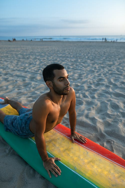 蓝色短裤的人坐在海滩上的红色和蓝色冲浪板 · 免费素材图片