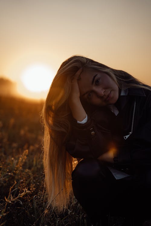 黑色皮夹克在日落时站在草地上的女人 · 免费素材图片
