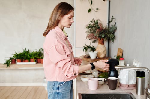 粉红色的衬衫和蓝色牛仔牛仔裤，站在褐色的木桌附近的女人 · 免费素材图片