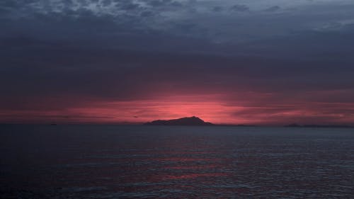 水体与日落时的一座山的轮廓视图 · 免费素材视频