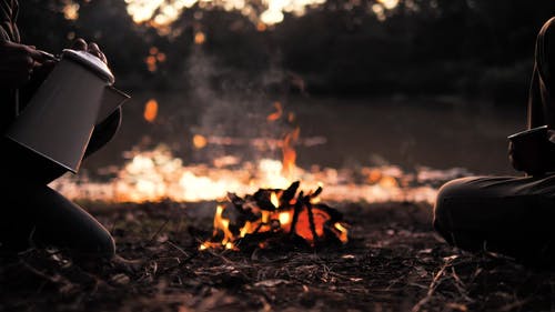 两人在篝火旁，从水壶里倒水 · 免费素材视频