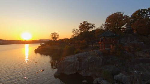 凉亭在岩层上的鸟瞰图，太阳落山背后的山脉反射在湖面上 · 免费素材视频