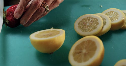 一个人在一个蓝色的砧板上切新鲜的草莓和柠檬的慢动作镜头 · 免费素材视频