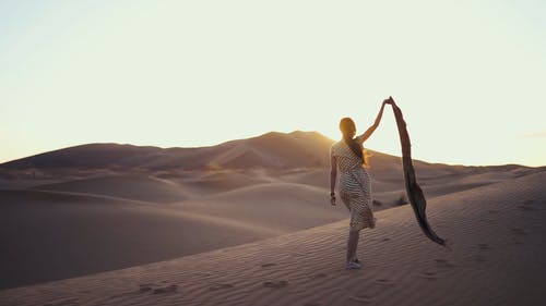 一个女人在大风天赤脚走在沙漠的沙子上举起她的围巾的手臂的慢动作镜头 · 免费素材视频