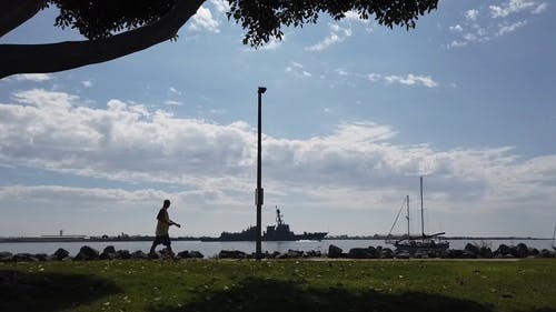 一个人在湾边散步，看着一艘船在港口内航行 · 免费素材视频