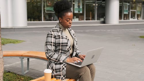 一个坐在户外长凳上的女人在笔记本电脑上工作时喝咖啡 · 免费素材视频