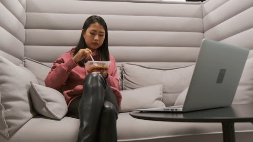 一个女人在沙发上吃饭时监视她的笔记本电脑 · 免费素材视频