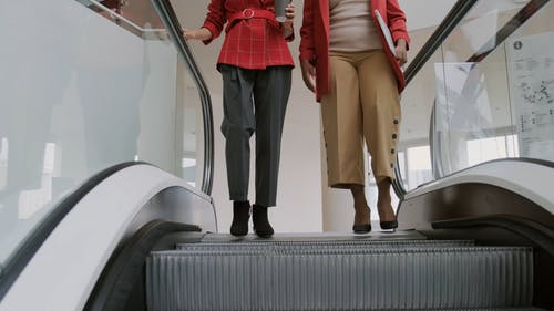 两名妇女踩着自动扶梯走到展厅时互相交谈 · 免费素材视频