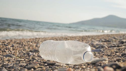 废弃的塑料瓶在岩石海岸与海浪在慢动作中的特写 · 免费素材视频
