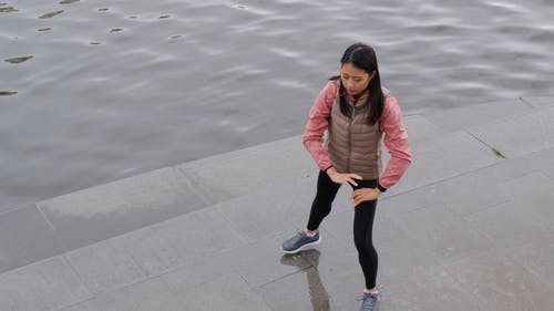 一个女人做身体伸展运动，沿着河岸 · 免费素材视频