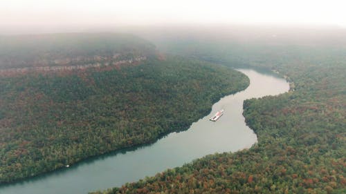 穿越茂密的森林和高山包围的一条河的驳船的航拍画面 · 免费素材视频