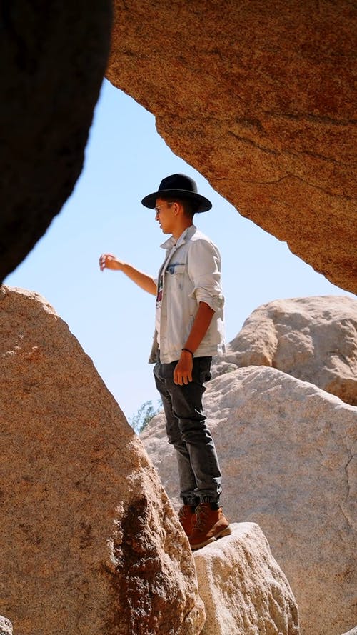 记录一个男孩站在岩石形成间隙中的一块巨石上 · 免费素材视频