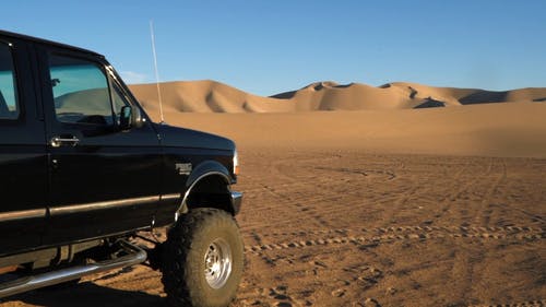 在白天用两辆车停在平坦干旱的地面上平移沙漠中沙丘和山脉的画面 · 免费素材视频