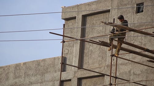 一名建筑工人在建筑物外部固定钢棚架的低角度镜头 · 免费素材视频