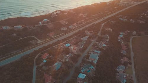空中的镜头，一条道路和房屋靠近海滨，地平线上有太阳落在海岸线的边缘 · 免费素材视频