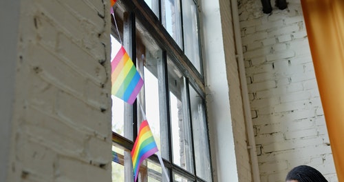把彩虹旗 Banderitas 放在窗玻璃上的女人 · 免费素材视频