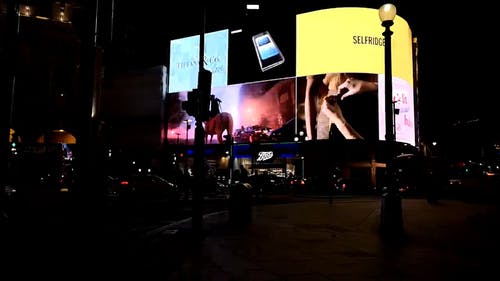 电子广告牌的巨型屏幕在漆黑的夜晚照亮了伦敦的一条街道 · 免费素材视频