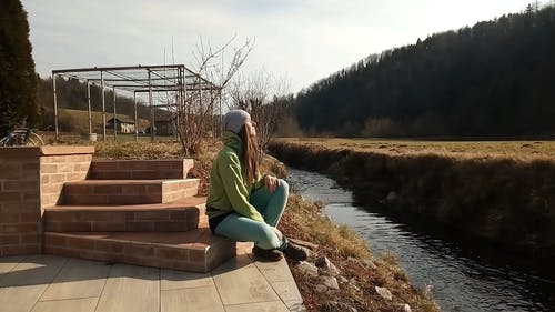 穿绿色夹克的女人试图在河边沉思 · 免费素材视频