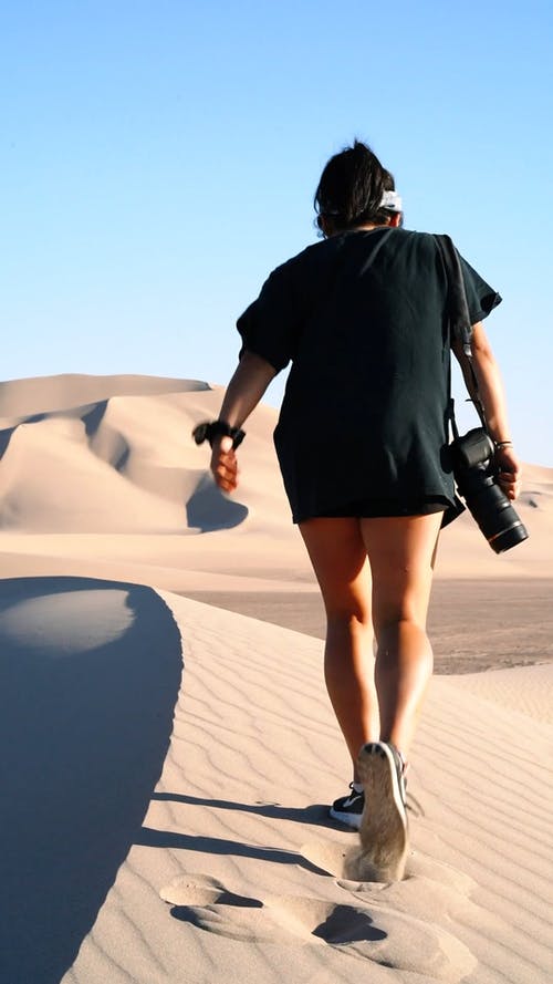 一个女人走在用相机的沙质沙漠上的手 · 免费素材视频