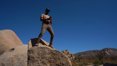 一个人站在一块大石头上以自拍照以沙漠景观为背景的低角度镜头 · 免费素材视频