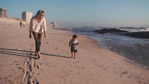 一位母亲和孩子在海滩岸边跑步 · 免费素材视频