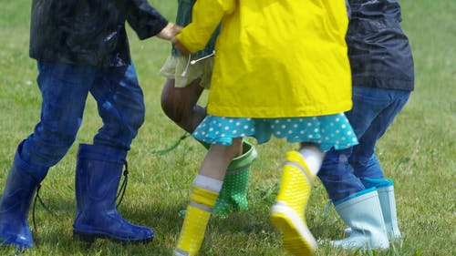 孩子们穿着防水靴子在雨下的草地上玩耍 · 免费素材视频