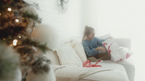 一个女孩坐在沙发上撕掉礼物包装纸从礼物 · 免费素材视频