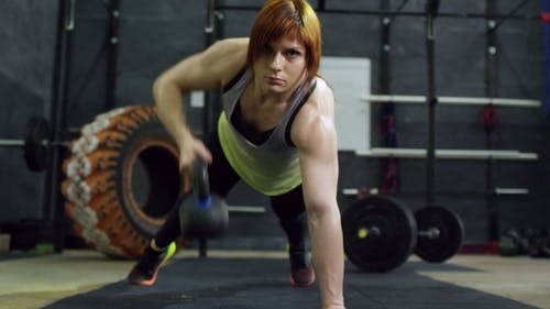 一个女人在俯卧撑锻炼姿势时举起铸铁水壶的重量 · 免费素材视频