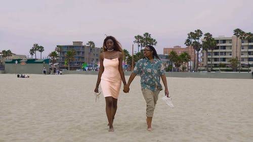 妇女夫妇牵着手在沙滩上散步 · 免费素材视频