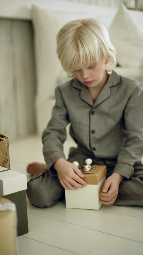 一个男孩试图打开一盒礼物 · 免费素材视频