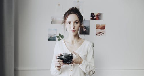 一个女人拿着照相机站在墙前与粘贴的图片 · 免费素材视频