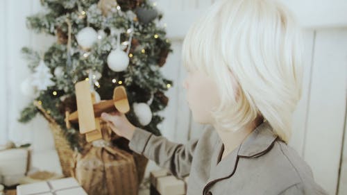 一个男孩在圣诞树旁玩木制玩具飞机 · 免费素材视频