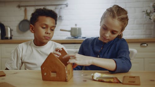 一个男孩看着一个女孩试图做一个由饼干制成的样板房 · 免费素材视频